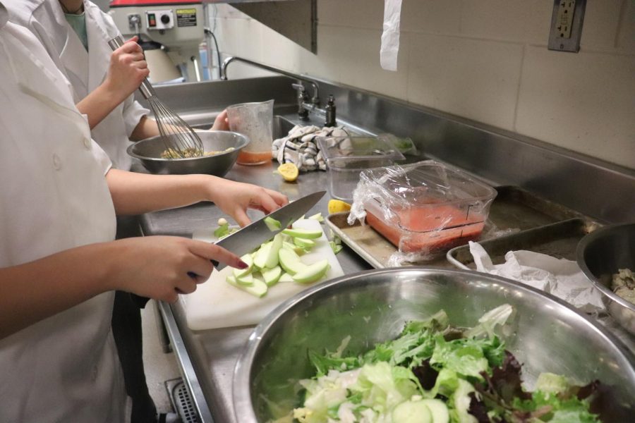 Freshman culinary students mixing together and cutting up ingredients for a salad. This unit in their learning works with creating varieties of salads along with dressings that they will be graded on.